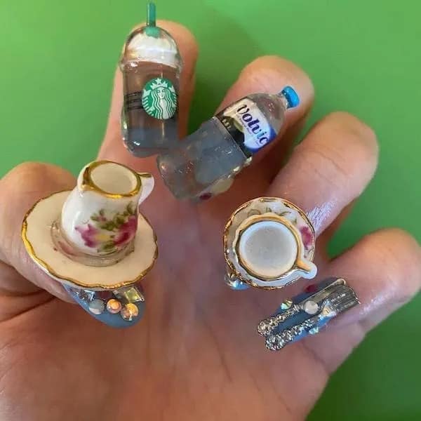 A funny meme of "cringe" 3D nail art, featuring a full teacup set, a Starbucks cup, and a Volvic bottle.