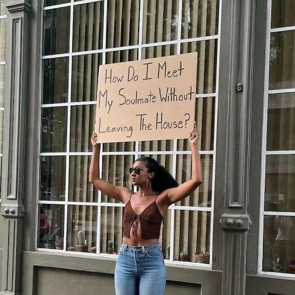 Woman holding a cardboard sign about meeting soulmates at home in a memes about being single.