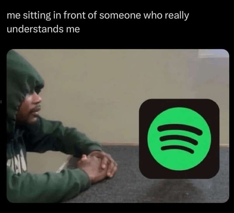 Man sitting alone at a table staring at the Spotify logo in a music meme.
