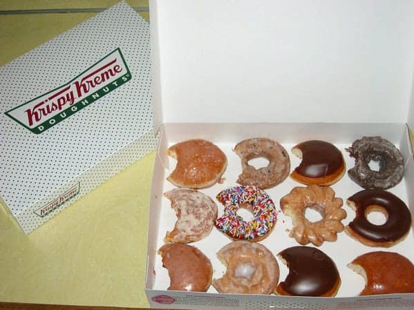 A box of a dozen Krispy Kreme donuts, where a single bite has been taken from every single one.