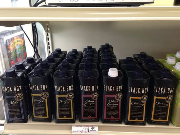A store shelf of Black Box wine, where one box has a white cap, ruining the perfect black cap display.
