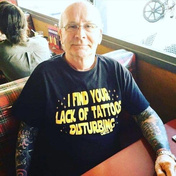 An older man with full tattoo sleeves, wearing a funny "Star Wars" shirt that says "I find your lack of tattoos disturbing."