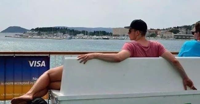 Confusing optical illusion photo where a man on a bench appears to have very muscular, bare female legs.