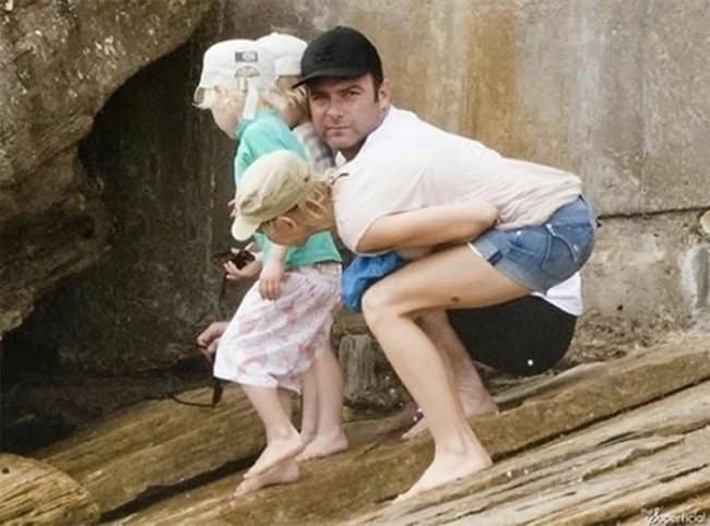 Confusing optical illusion photo of Liev Schreiber appearing to have a woman's body with bare legs and jean shorts.