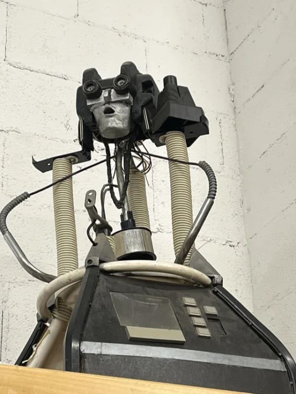 Broken industrial robot head looking like a sad human face with wires hanging.