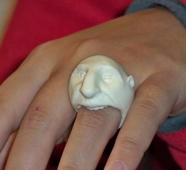 A creepy and weird ring designed as a grotesque white face that appears to be biting the wearer's finger.