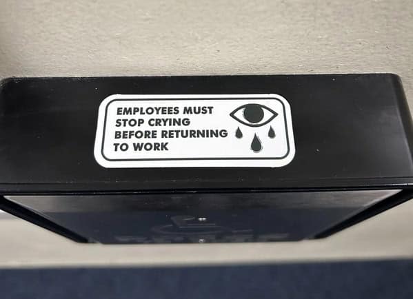 A funny, dystopian sticker on a machine that reads "Employees must stop crying before returning to work."