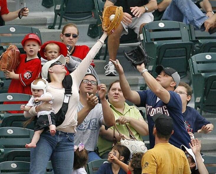 An accidental renaissance painting image of fans at a baseball game reaching for a foul ball while holding babies.