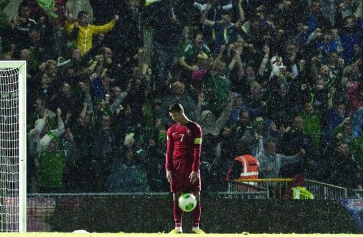 An accidental renaissance painting photo of a soccer player standing alone in the rain with a cheering crowd in the background