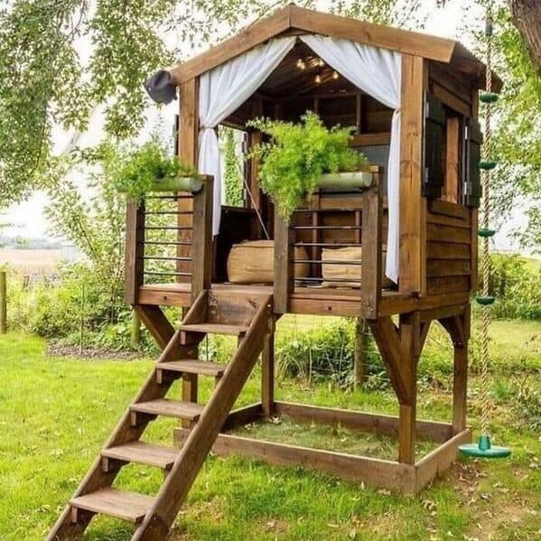 An amazing woodworking treehouse with a balcony and curtains in a backyard