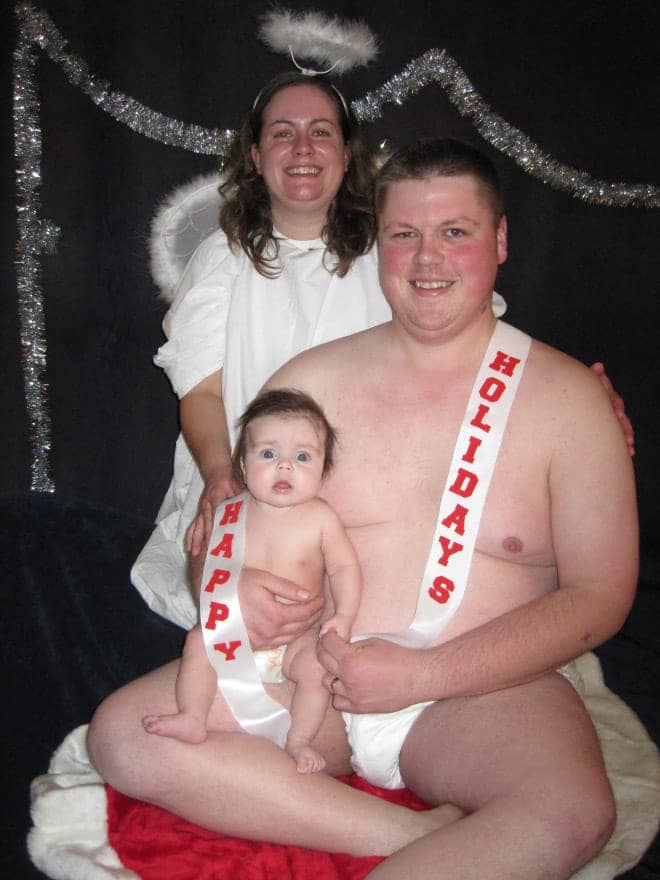 In this awkward family christmas photo, a man wears a diaper and a holiday sash next to a real baby