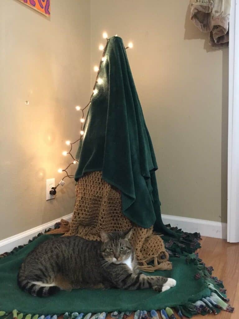 A cat christmas tree completely covered in a green blanket to prevent climbing.