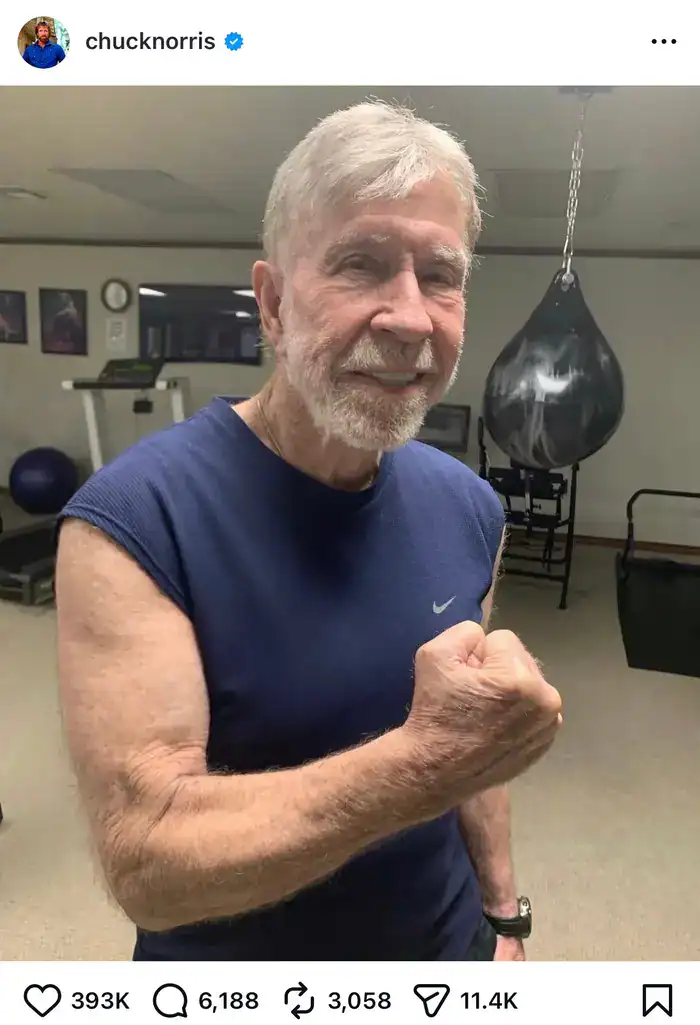 A photo of an older Chuck Norris smiling and flexing his bicep in a gym.