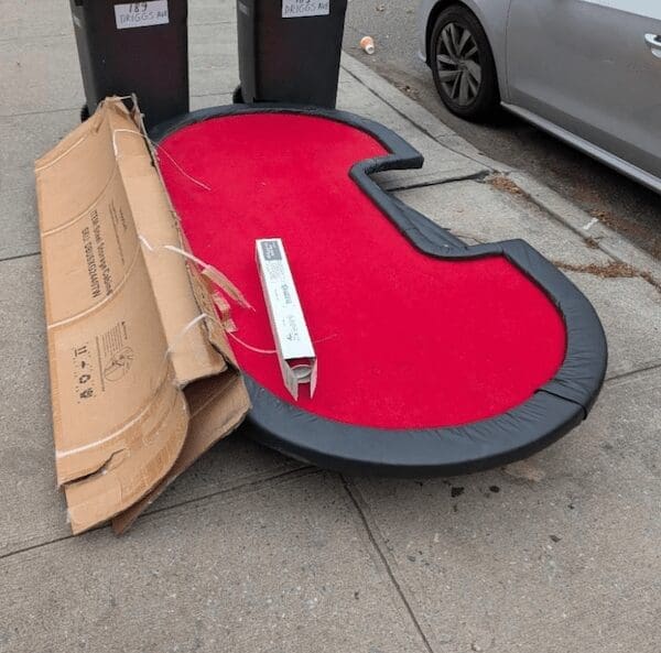 A funny curb find of a red poker table top sitting next to trash cans.