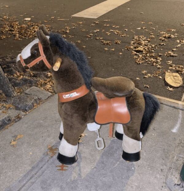 A funny curb find of a brown plush ride on horse toy on the sidewalk.