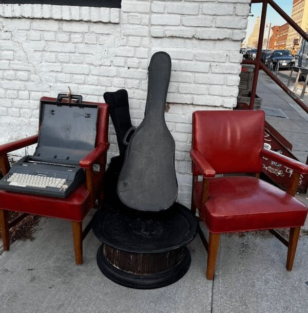 A curb alert collection of red chairs a typewriter and a guitar case.