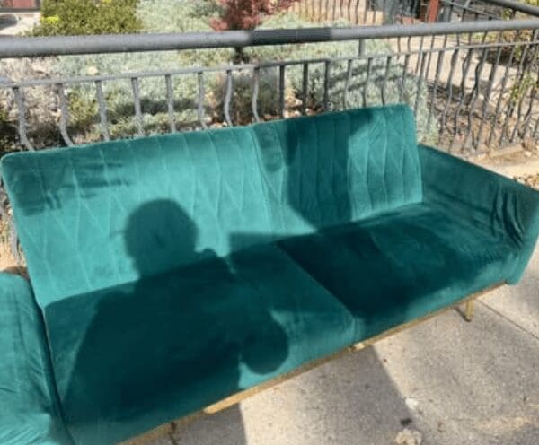 A curb alert photo of a green velvet sofa sitting outside on the pavement.