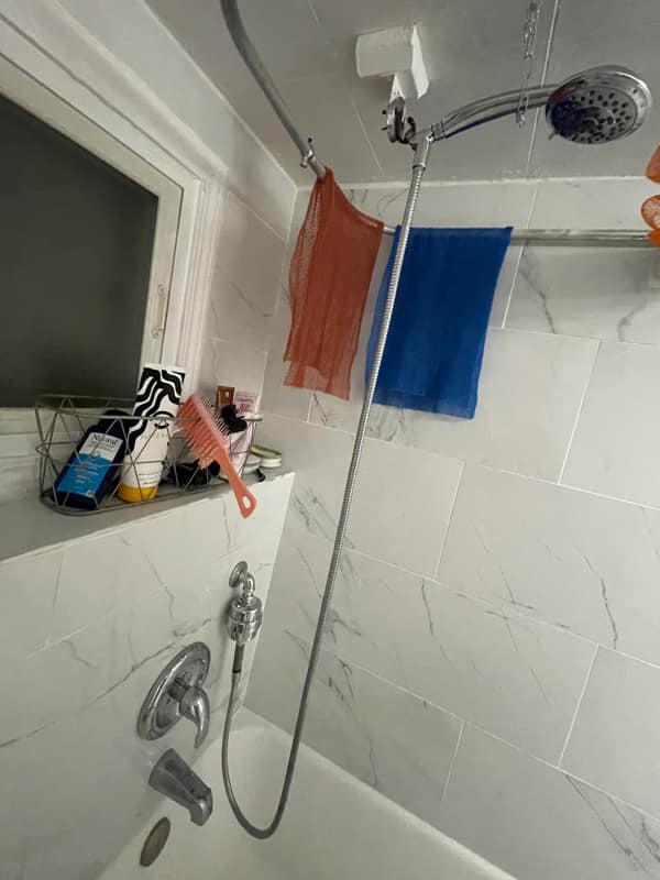 A diy fail shower head installation using an overly long flexible pipe hanging from the ceiling.