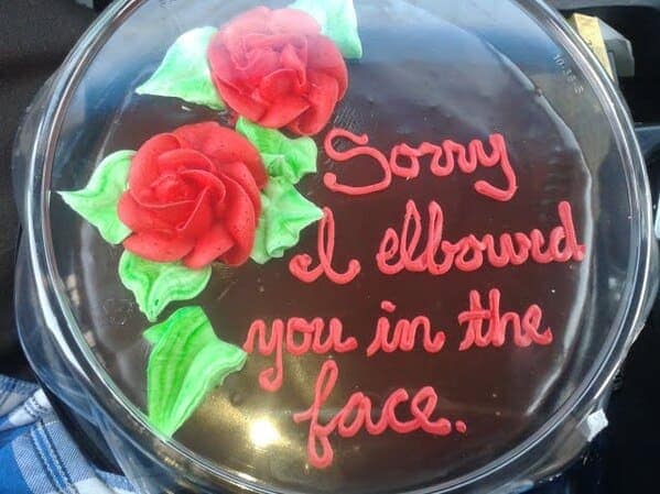 Chocolate cake with roses apologizing for elbowing someone in the face.