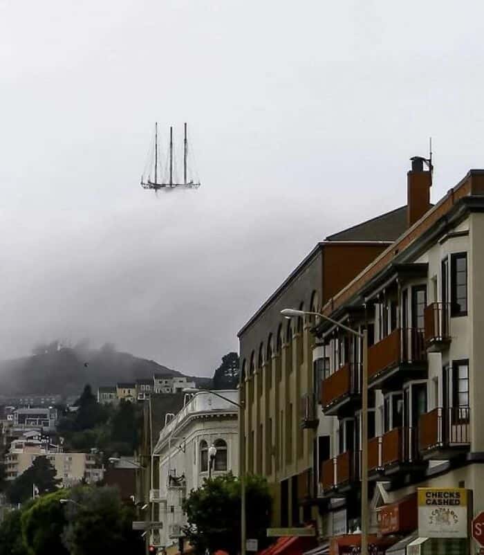 A funny optical illusion of a ship floating in the sky above fog.