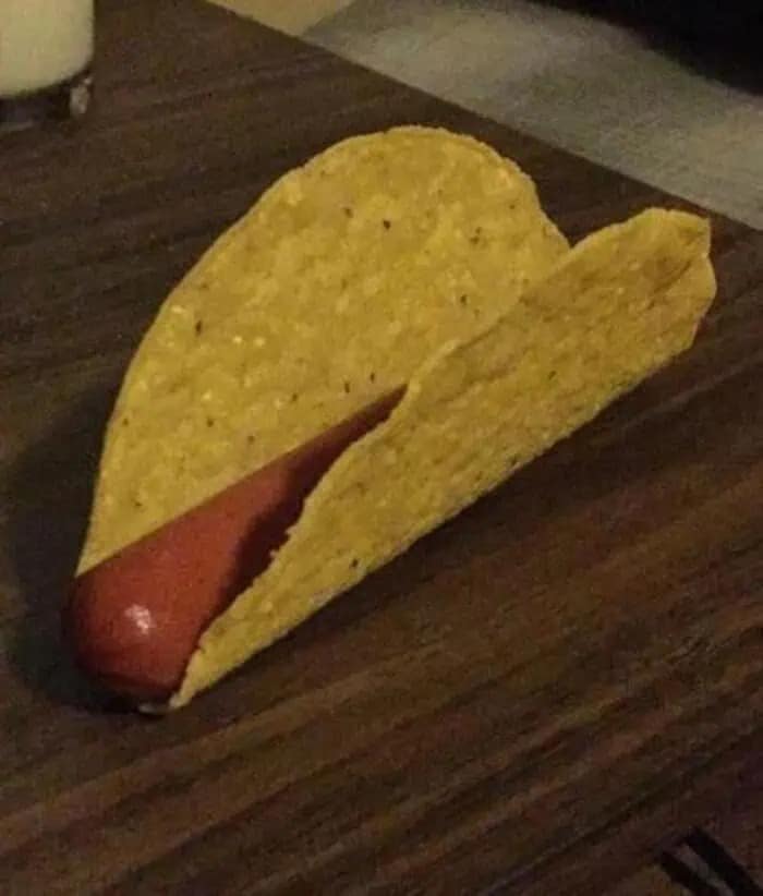 Hot dog sausage placed inside a hard taco shell cursed food image.