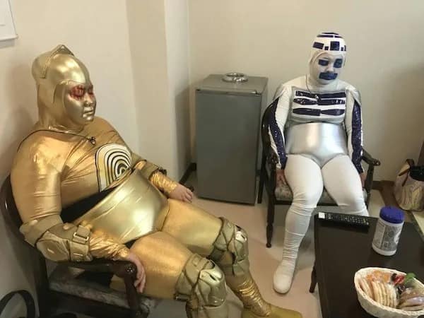 Two people wearing ill-fitting budget C-3PO and R2-D2 costumes sitting in waiting room.