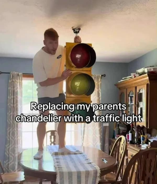 Man standing on dining table installing a large traffic light instead of a chandelier.