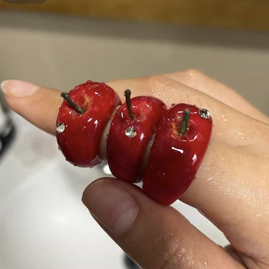 Three rings worn on fingers made to look like realistic miniature red apples.