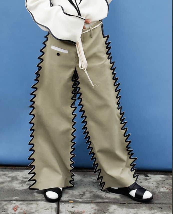 Person wearing beige trousers with exaggerated wavy black cutouts running down the legs.