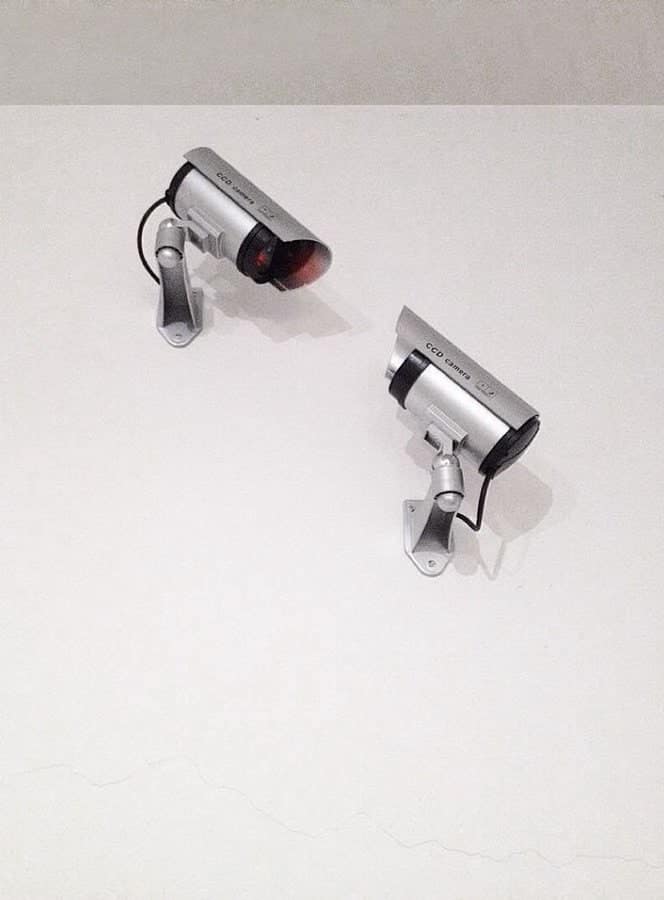 Two security cameras mounted on a white wall positioned to look like they are kissing.