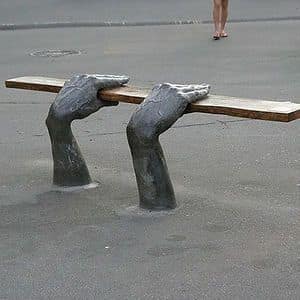 Park bench where the legs are sculpted to look like bronze hands holding the seat.