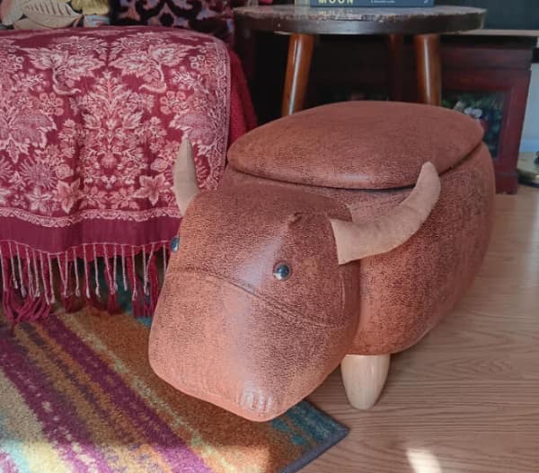 A funny thrift store find ottoman shaped like a brown bull with horns.