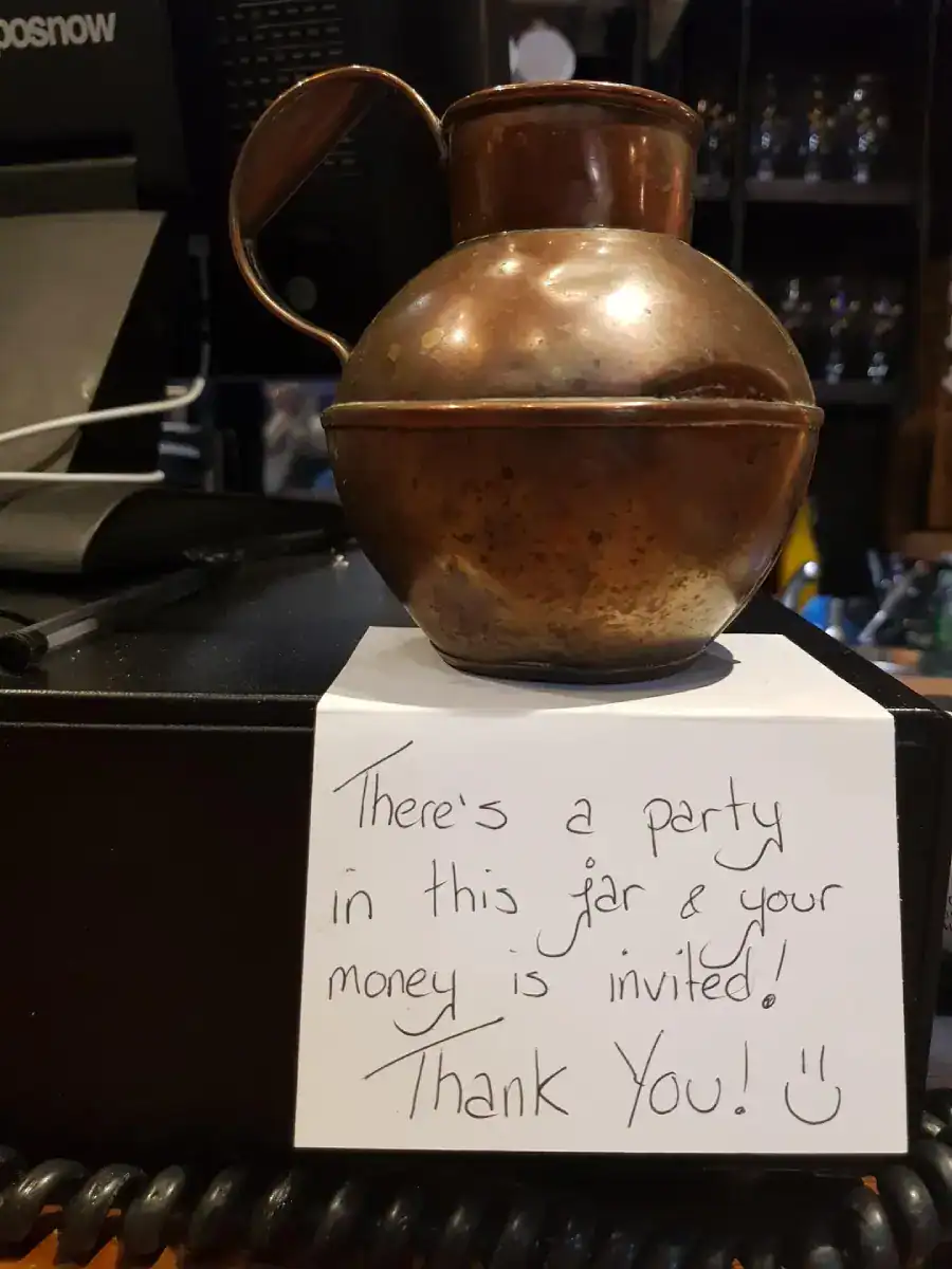 A creative tip jar copper pot inviting money to a party inside the jar.