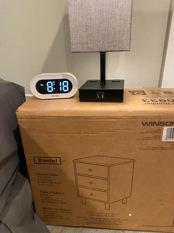Lamp and digital clock sitting on top of unopened nightstand cardboard box.