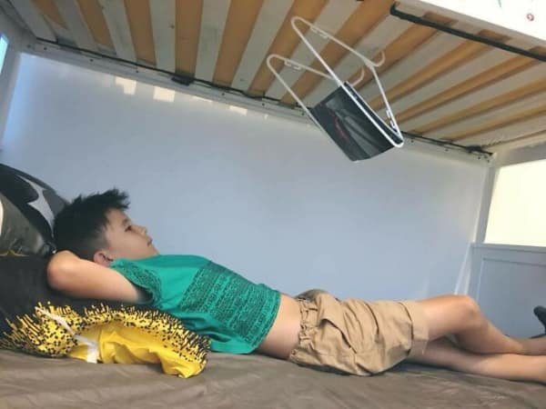 Child on bottom bunk watching tablet suspended by hangers from top bunk.