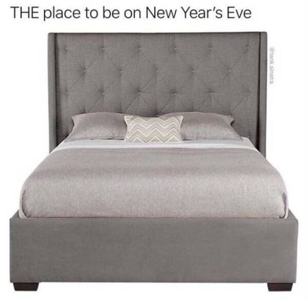A funny photo of a comfortable grey bed labeled as the place to be on New Years Eve.