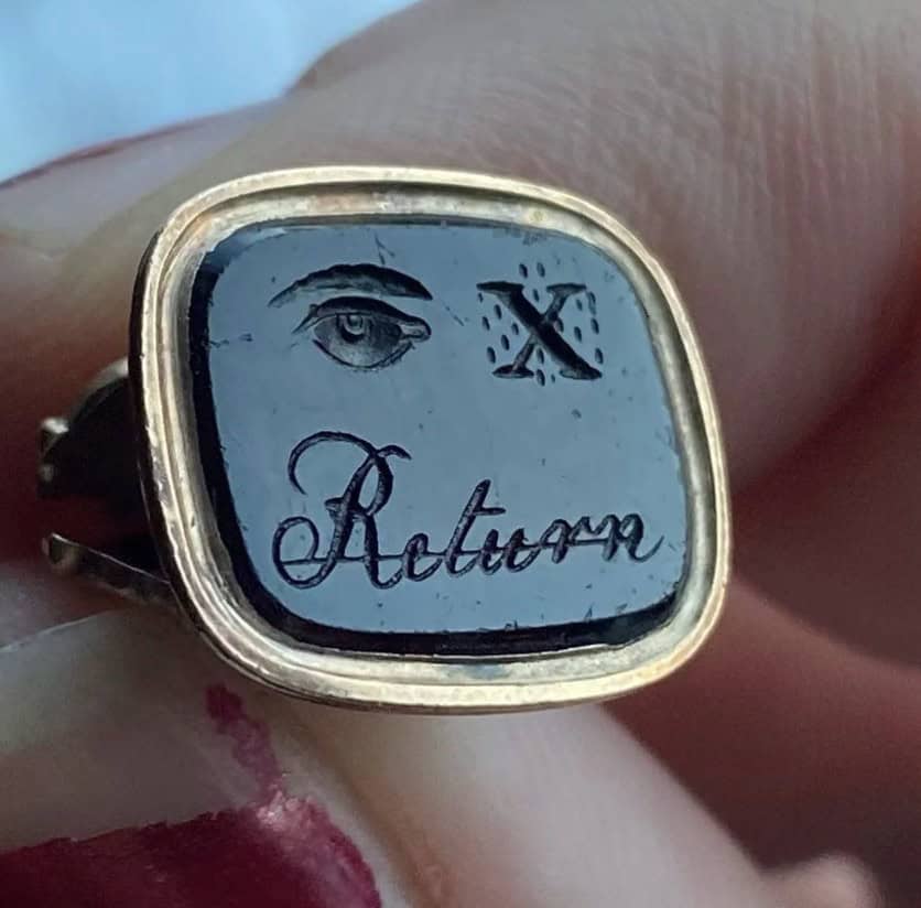 Gold ring with black face showing an eye letter X and word Return.