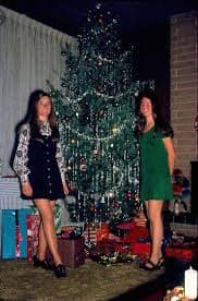 A retro christmas photo of two women standing by a tinsel covered tree.