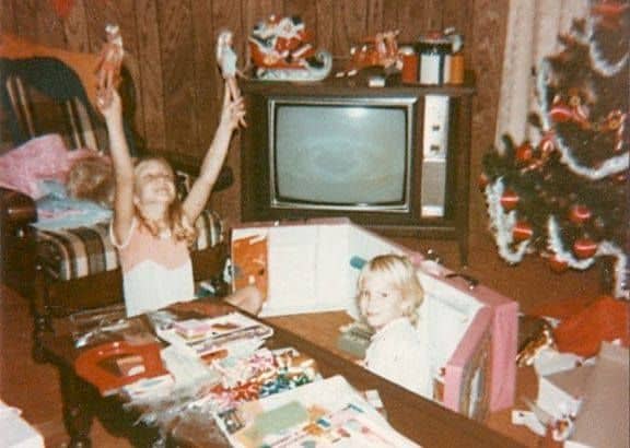 A retro christmas photo of a girl holding new Barbie dolls.