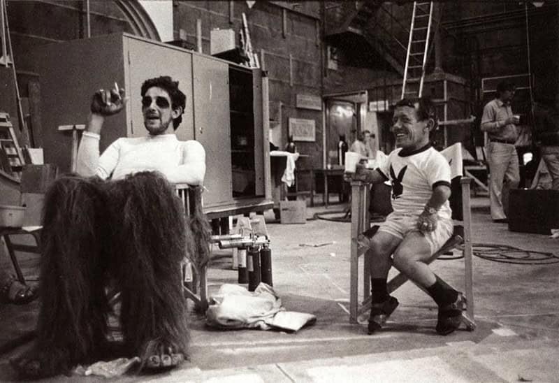 A Star Wars BTS photo of Peter Mayhew as Chewbacca smoking a cigarette next to Kenny Baker.