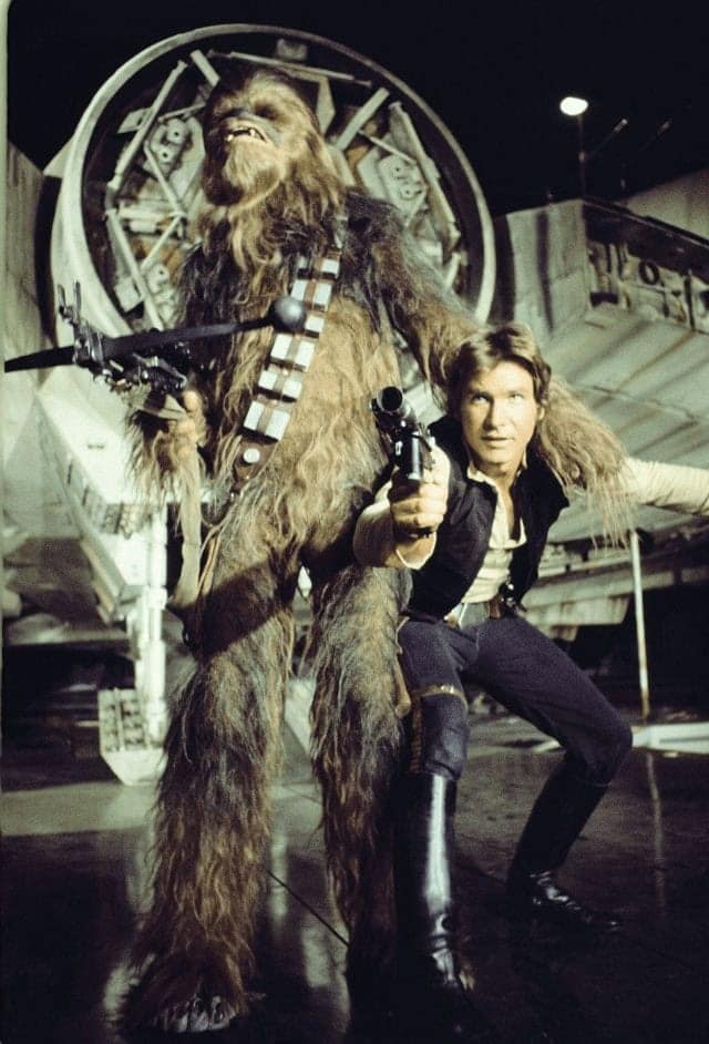 A Star Wars BTS photo of Han Solo and Chewbacca posing with Lando Calrissian peeking from behind.