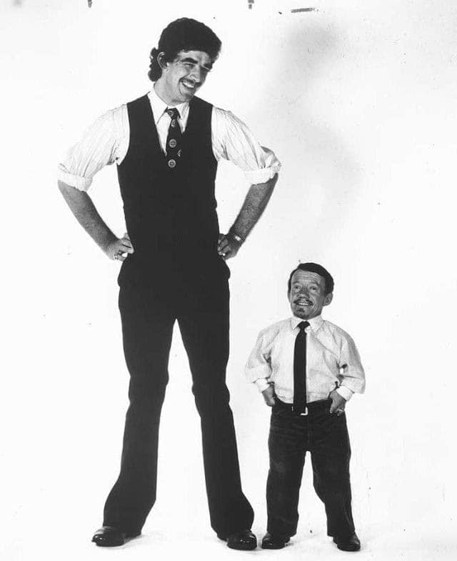 A Star Wars behind the scenes photo of Peter Mayhew and Kenny Baker standing side by side in street clothes.