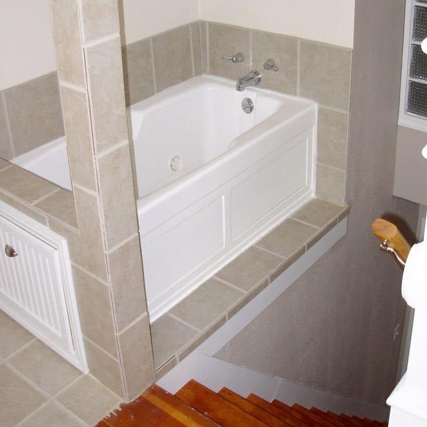 Bathtub installed directly next to a staircase with a tiled barrier ledge.