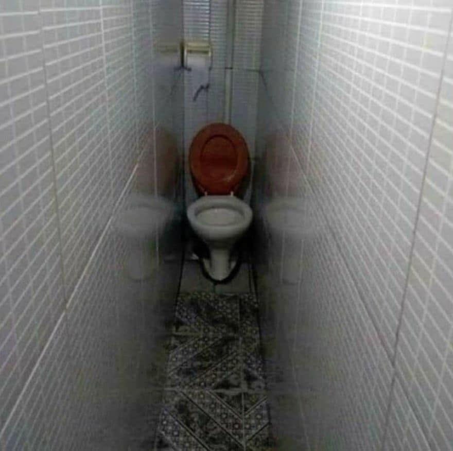 Extremely long and narrow tiled bathroom with a toilet at the very end.