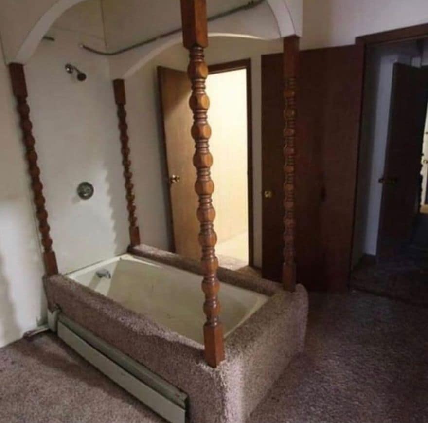 Bathtub with a wooden four-poster frame sitting on carpet in a bedroom.