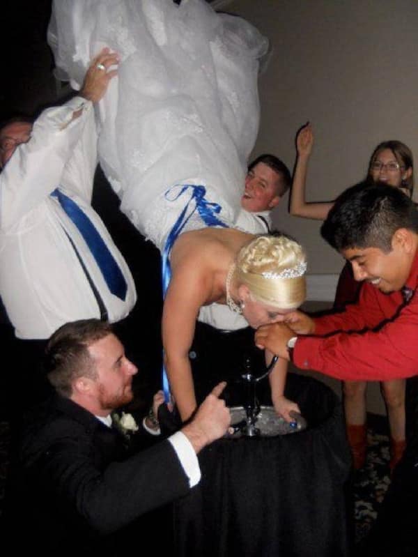 Bride being held upside down doing a keg stand in her wedding dress.