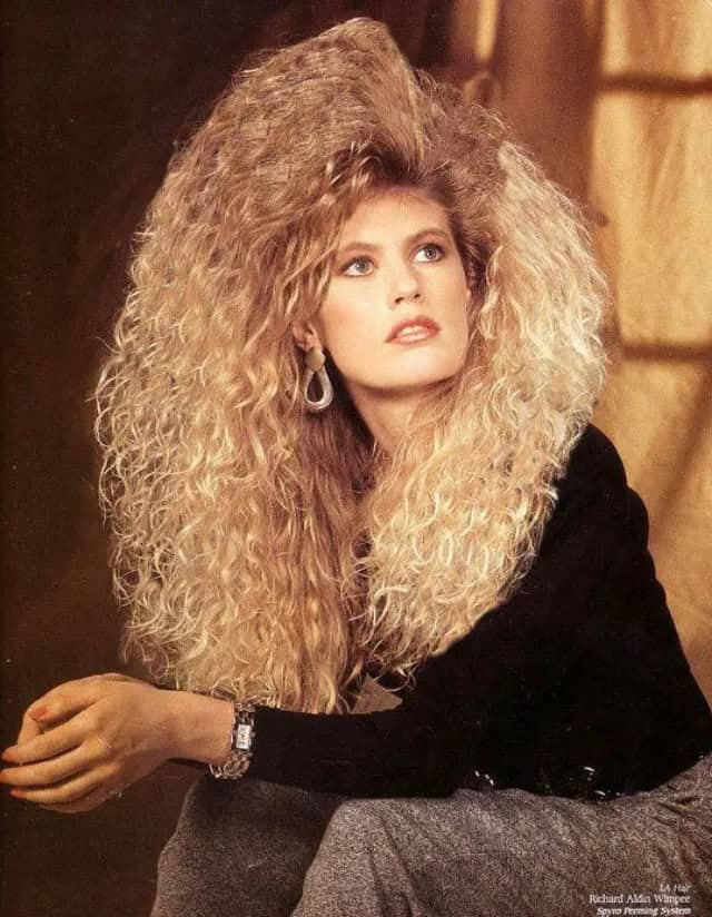 A blonde model showing off a triangular 80s haircut with extreme volume on the sides.