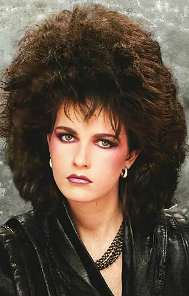 A woman with a dark, feathered 80s haircut blown out to create a wind-tunnel effect.