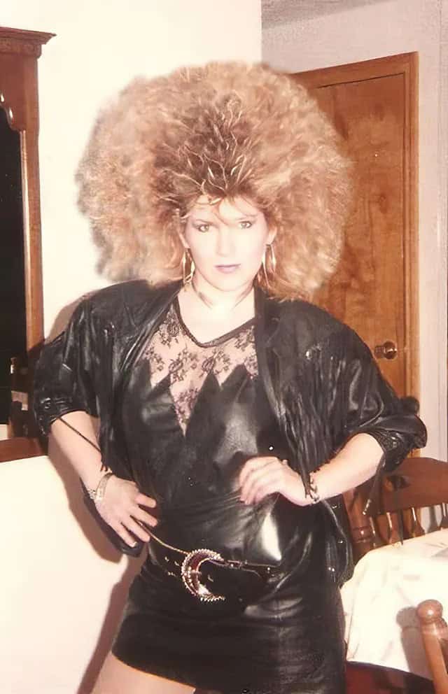 A woman in leather holding a purse with a frizzy, two-toned 80s haircut.