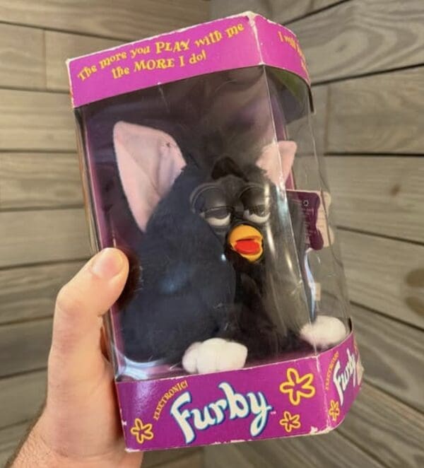 A black and pink Furby in its original purple box, the defining animatronic 90s toy.